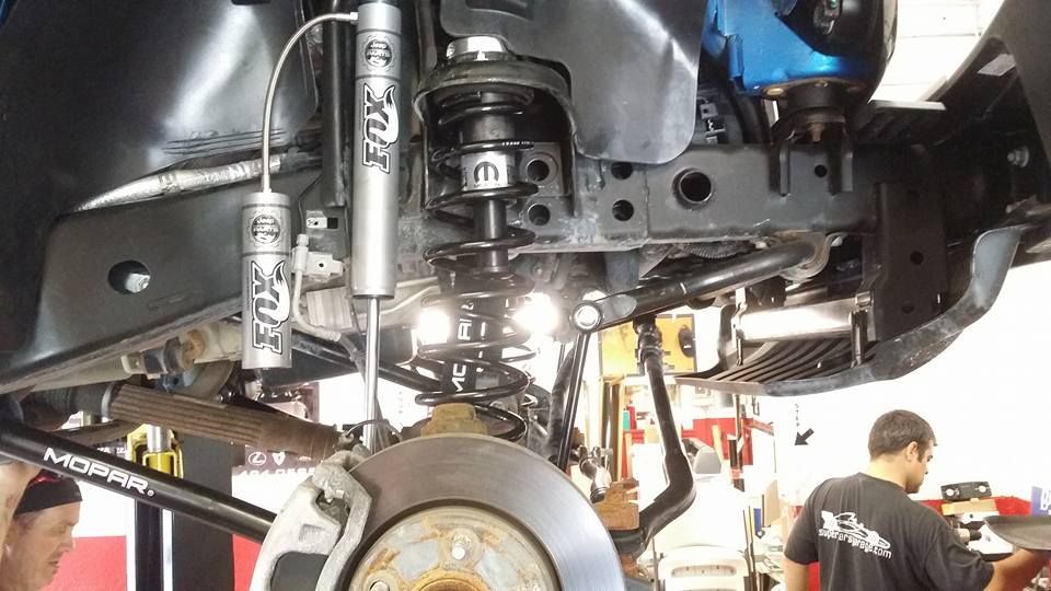 Jeep suspension with FOX shocks. Mechanic works under the vehicle. Shop setting.