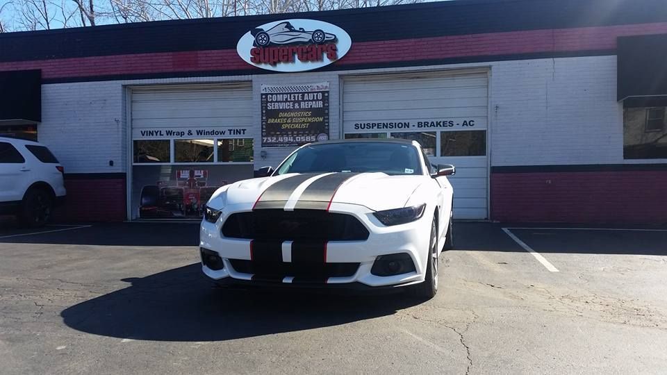 White Ford Mustang with black stripes parked in front of a car repair shop.