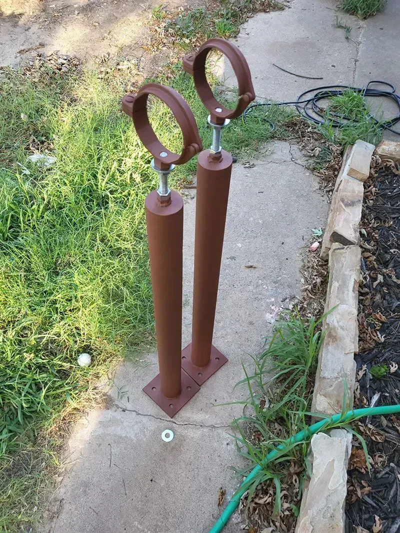 A pair of brown pipe clamps are sitting on a sidewalk next to a hose.