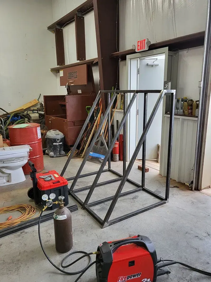 A welding machine is sitting in a garage next to a ladder.