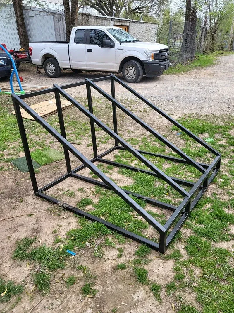 A white truck is parked next to a metal frame in the grass.