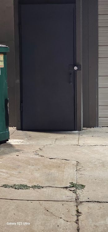 A black door is sitting on a sidewalk next to a green trash can.