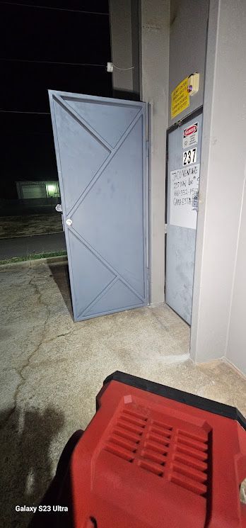 A red box is sitting in front of a door that is open at night.