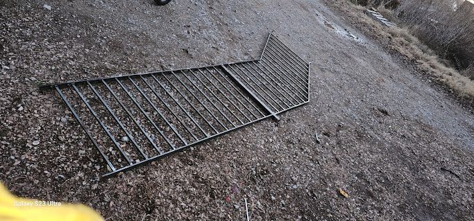 A metal fence is laying on the ground on the side of a road.