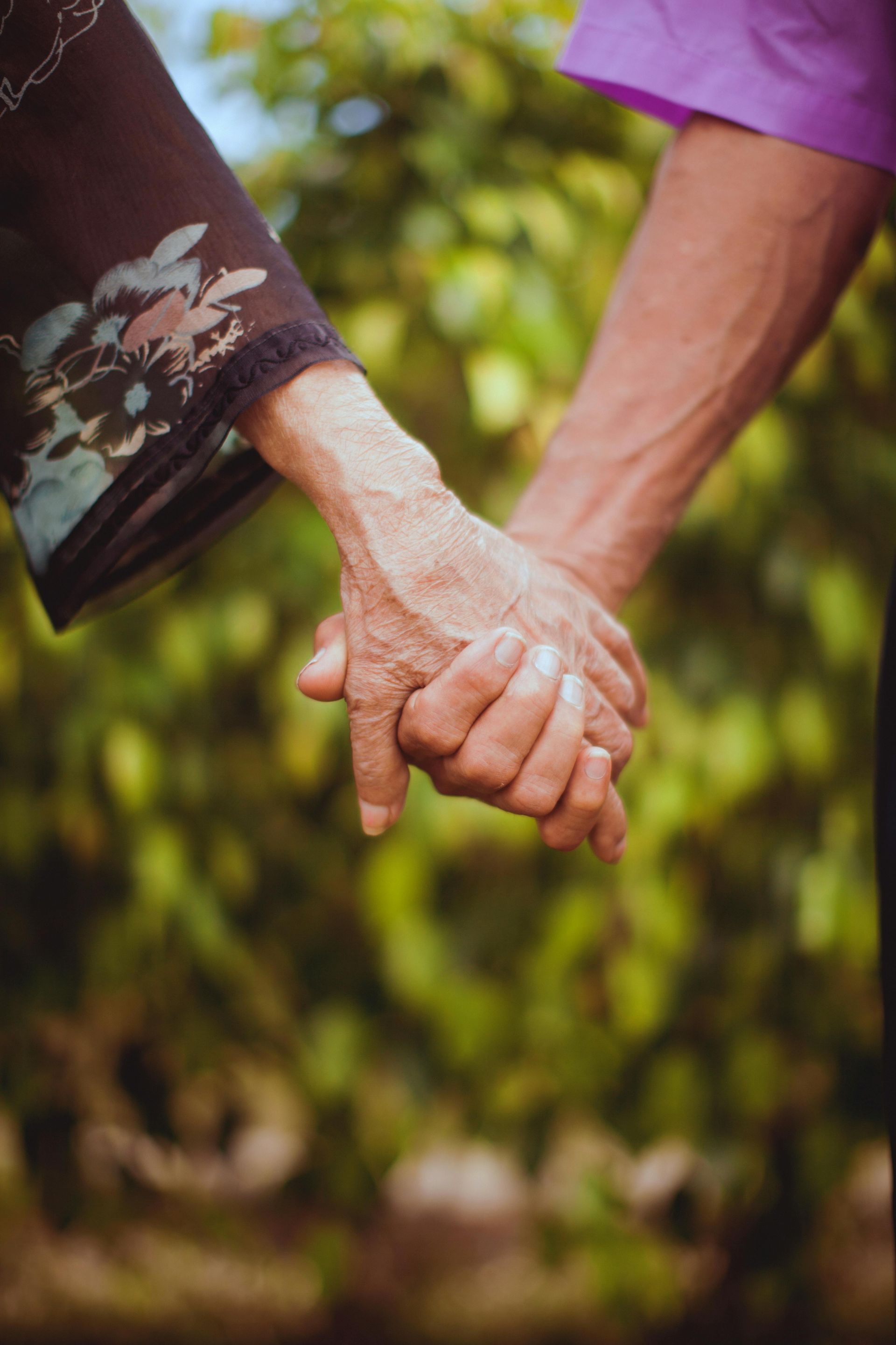 A man and a woman are holding hands in front of trees.