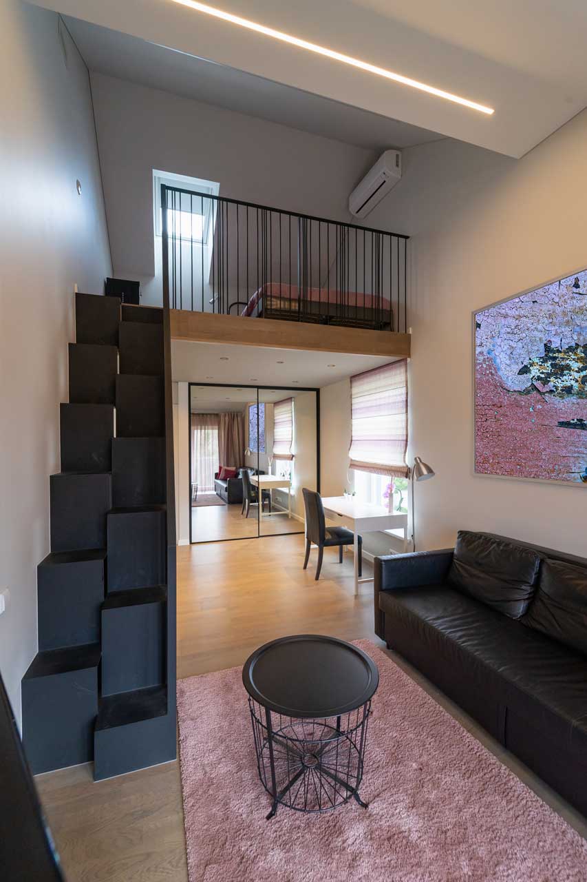 A living room with a couch , table , and stairs leading to a bedroom.