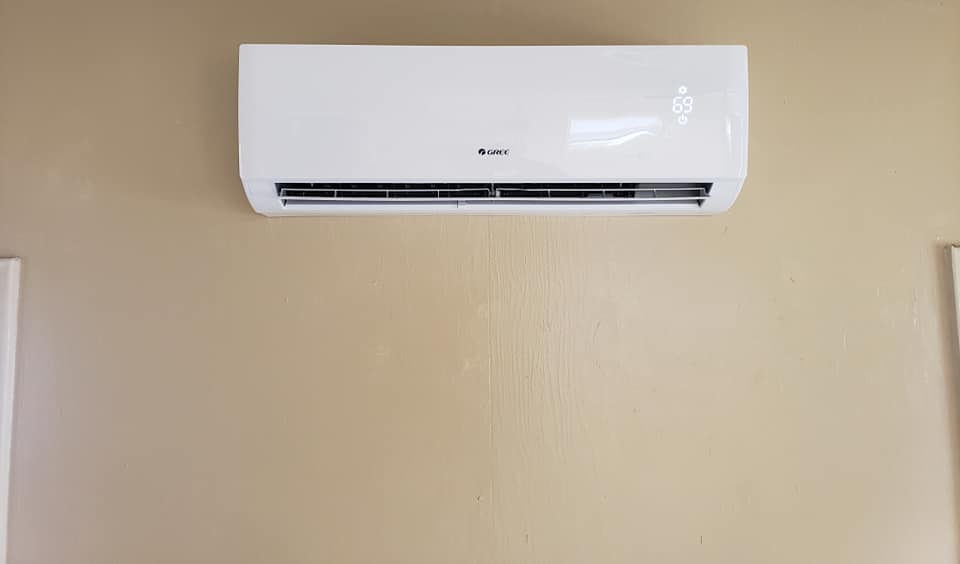 A white air conditioner is hanging on a tan wall.