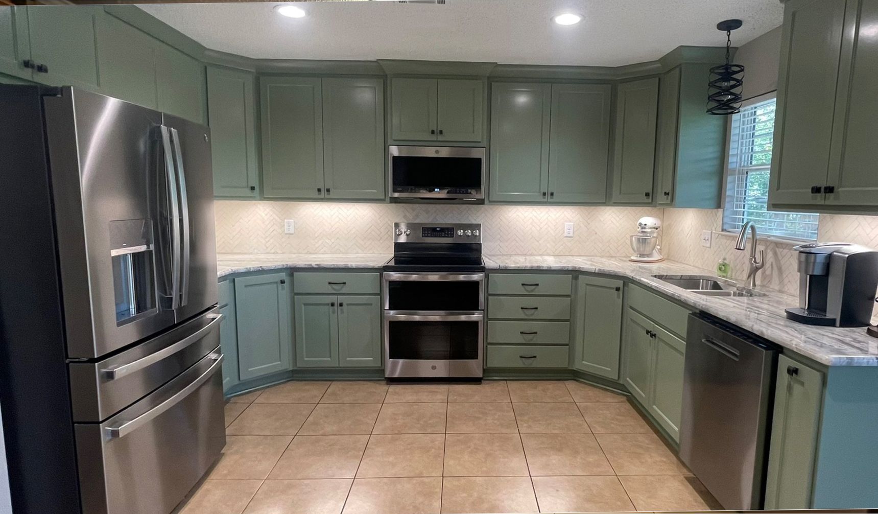 Green kitchen cabinets with stainless steel appliances and granite countertops.