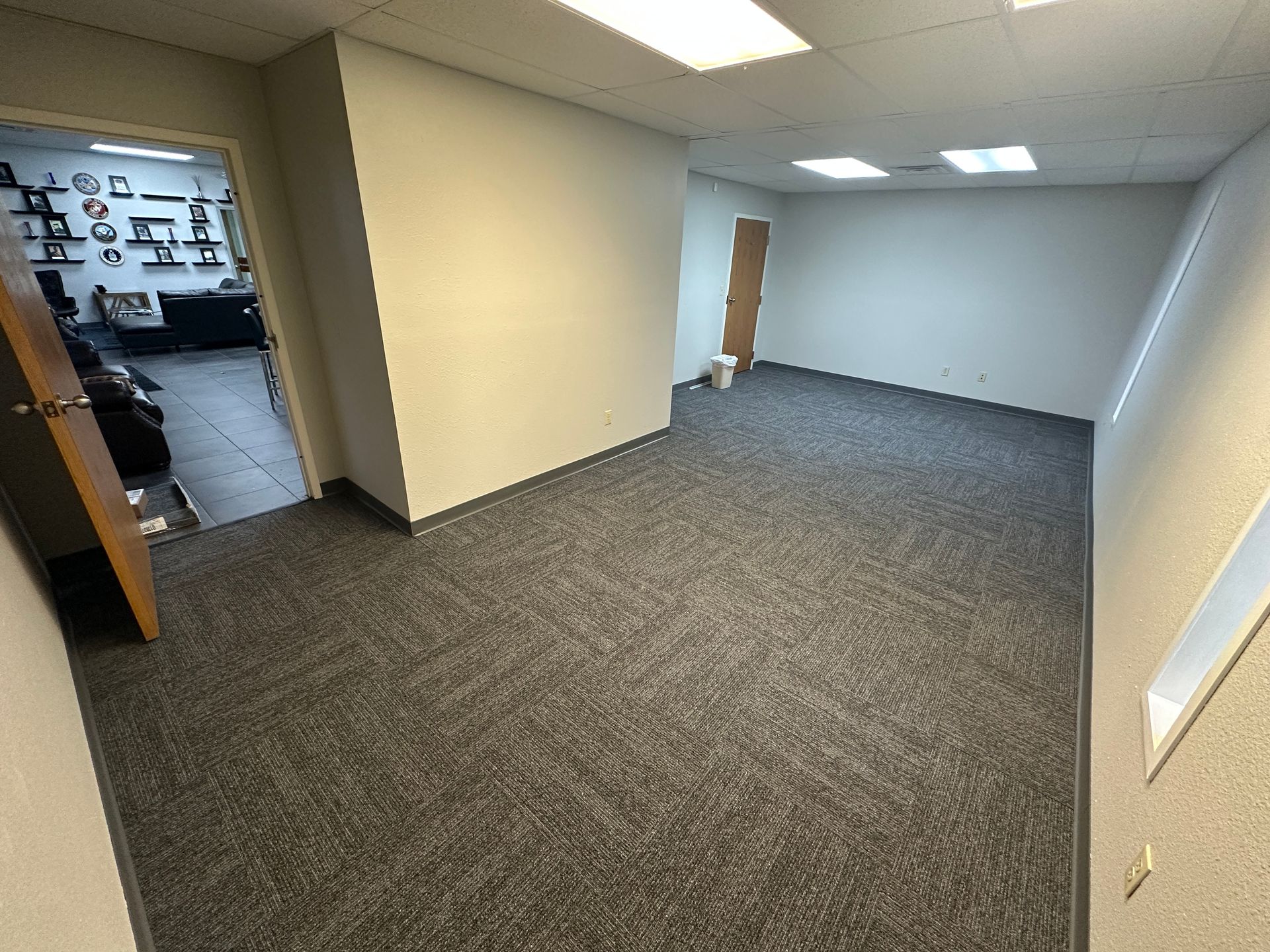 An empty room with a carpeted floor and a door leading to a living room.