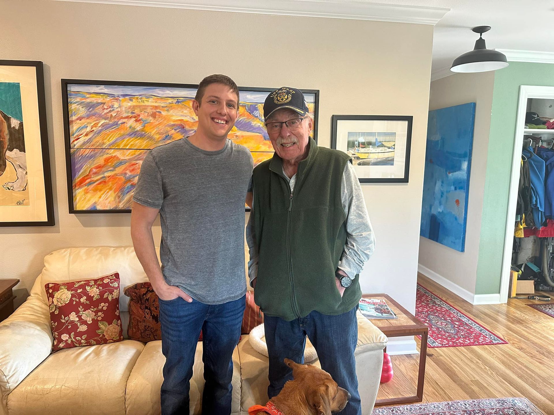 Two men and a dog are posing for a picture in a living room.