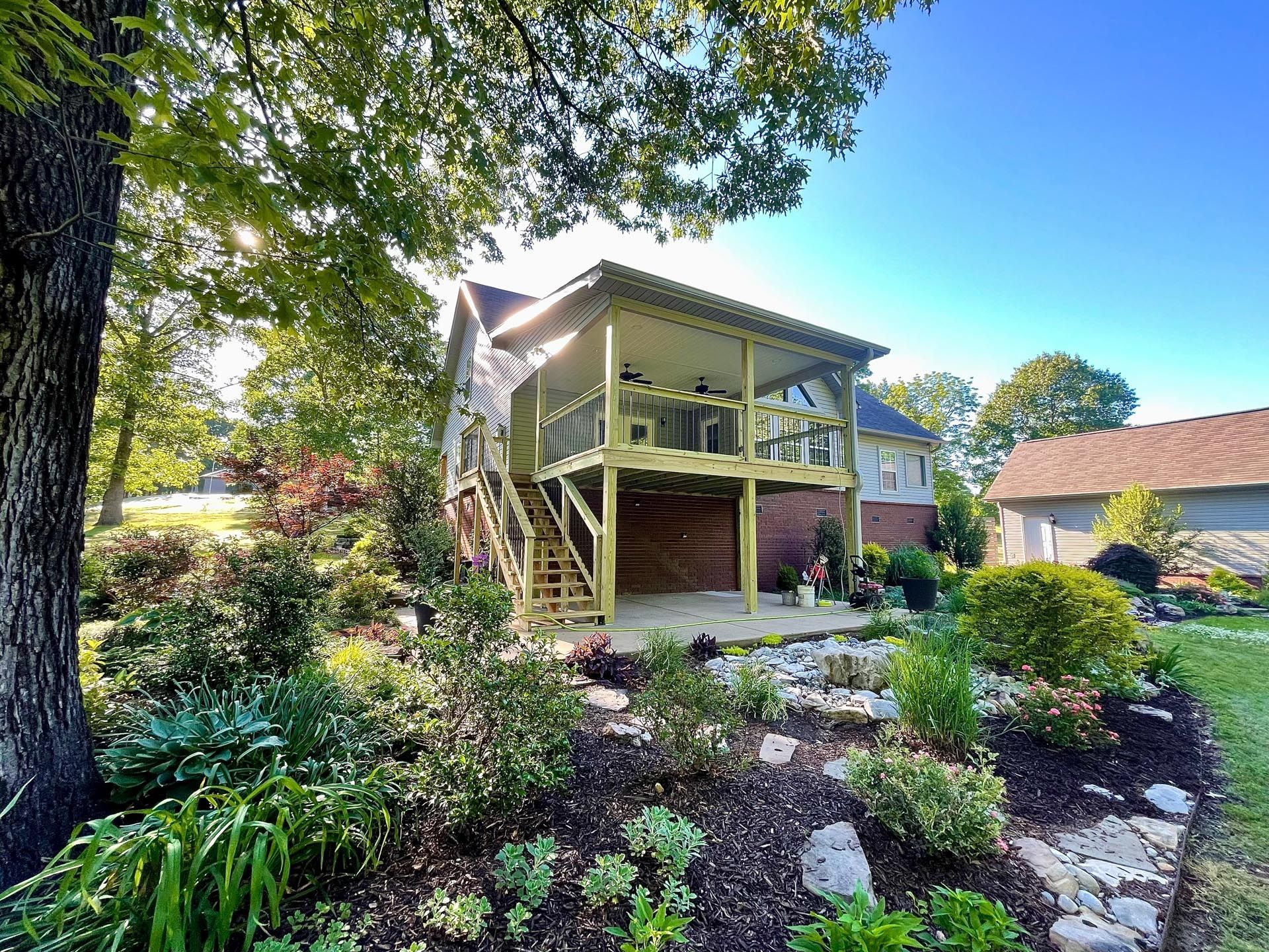 A house with a large deck and stairs surrounded by trees and bushes.