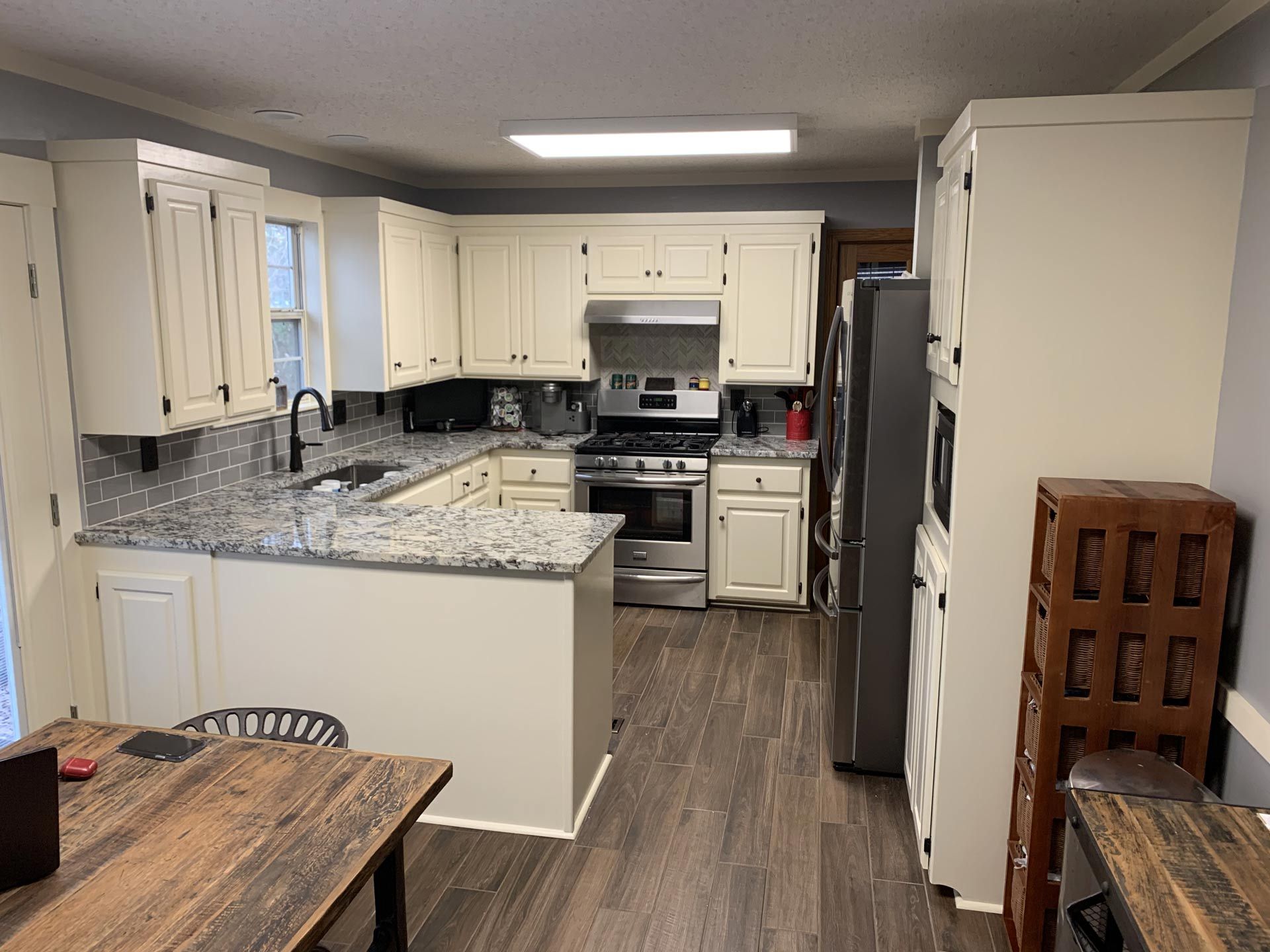 A kitchen with white cabinets , granite counter tops , stainless steel appliances and a wooden table.
