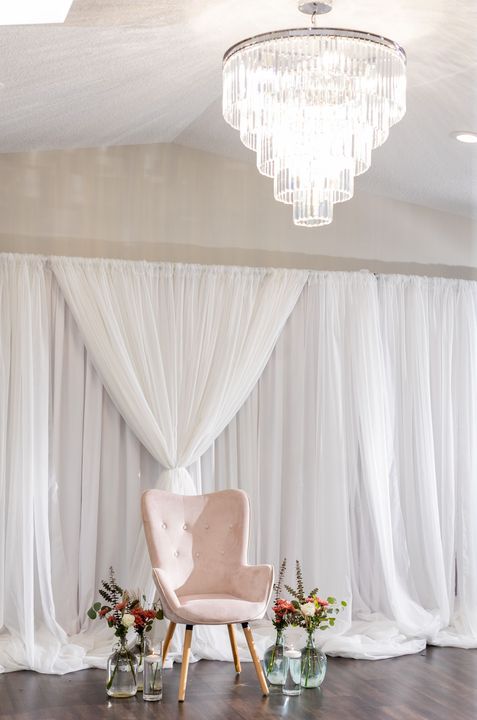 A pink chair is sitting in front of a white curtain.