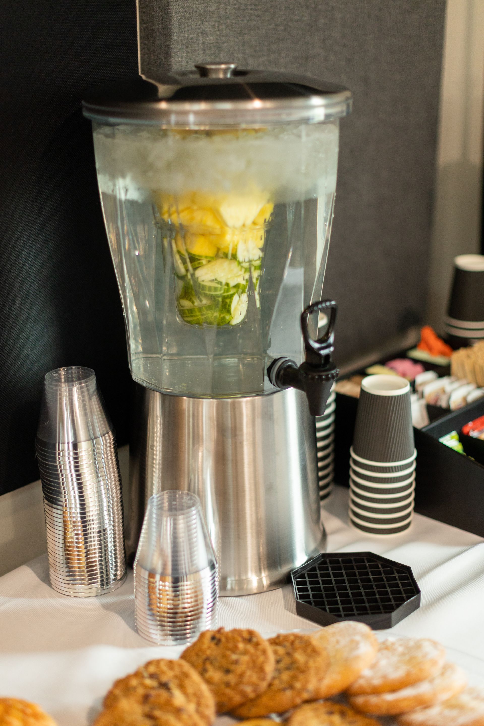 A beverage dispenser filled with water and lemon slices on a table.