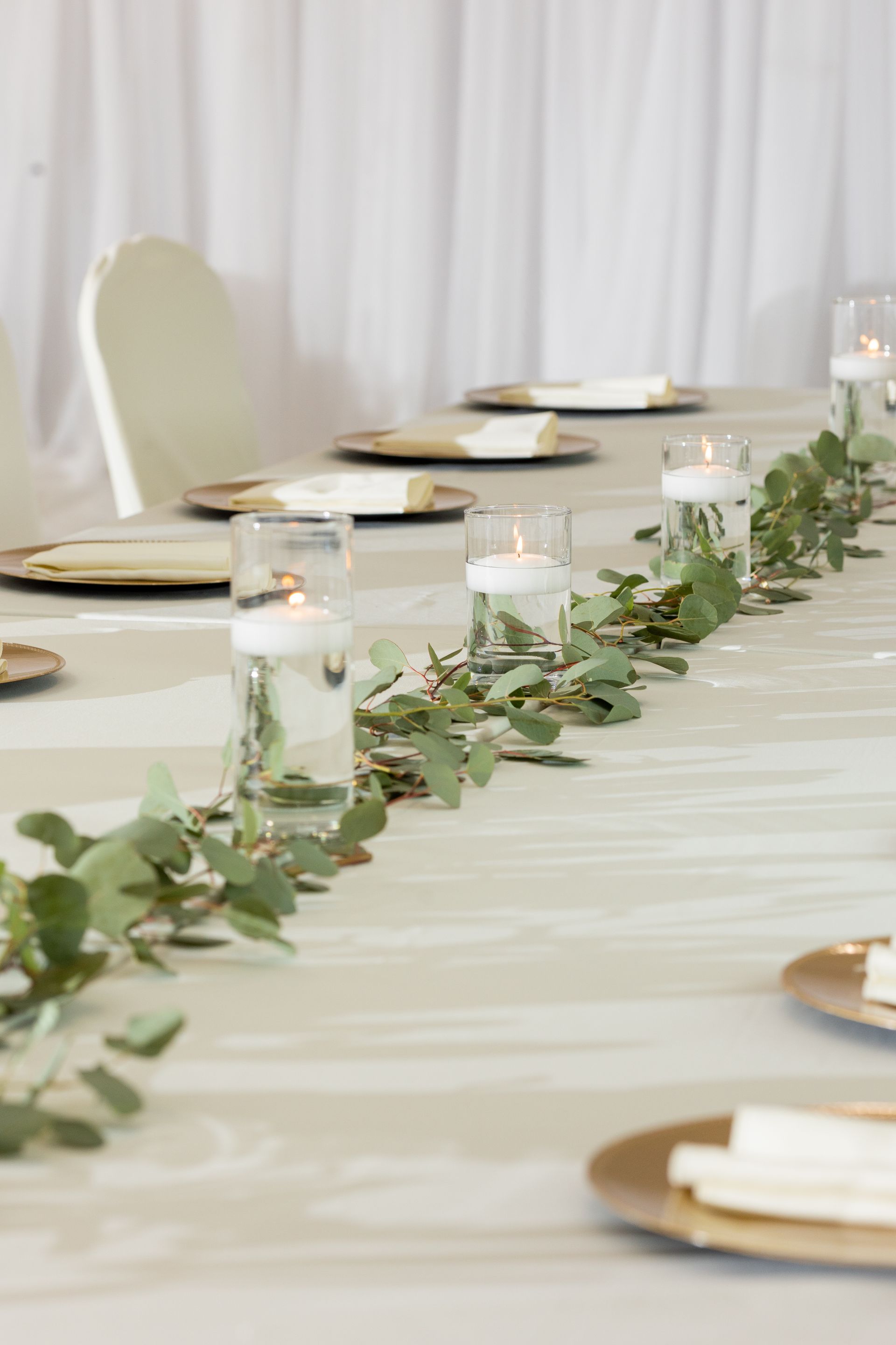 A long table with plates , candles , and greenery on it.