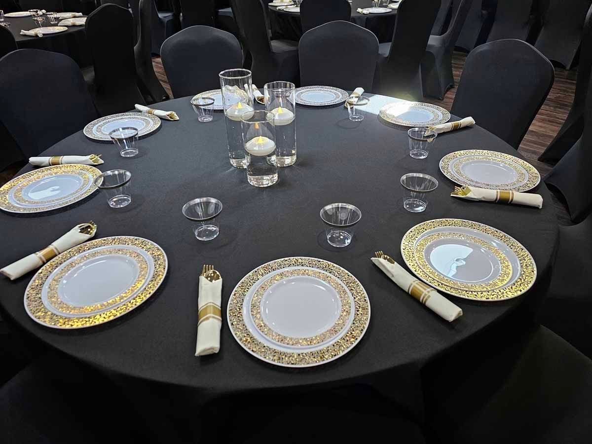 A round table with plates , napkins , glasses and candles on it.