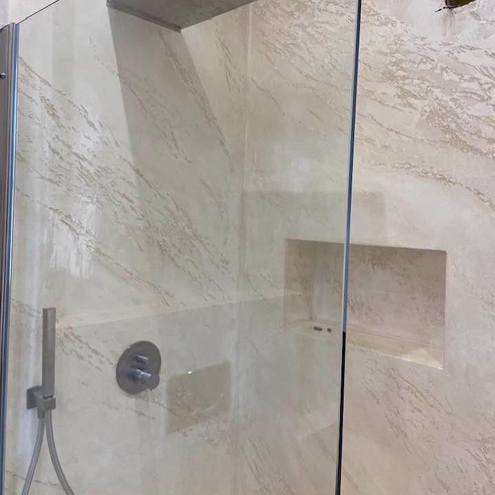 Box doccia in vetro con piastrelle color crema effetto marmo, soffione, maniglia e nicchia incassata integrata.