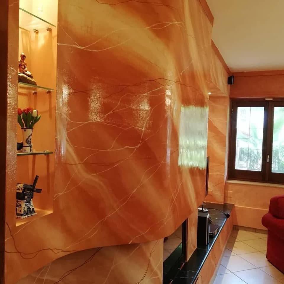 Una parete curva con finitura arancione effetto marmo e sottili venature bianche, caratterizzata da una mensola a incasso e profili scuri.