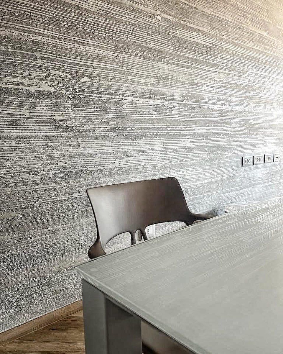 Una sedia moderna è posizionata accanto a un tavolo grigio chiaro, addossato a una parete con una trama che imita le venature del legno.