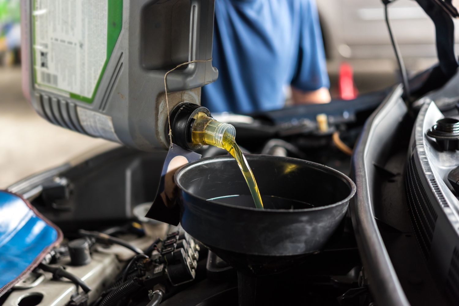 Oil pouring from a container into a funnel in a car engine compartment