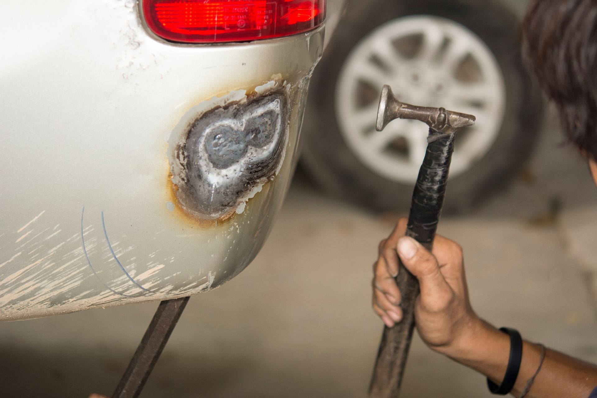 A man is using a hammer to fix a car bumper.