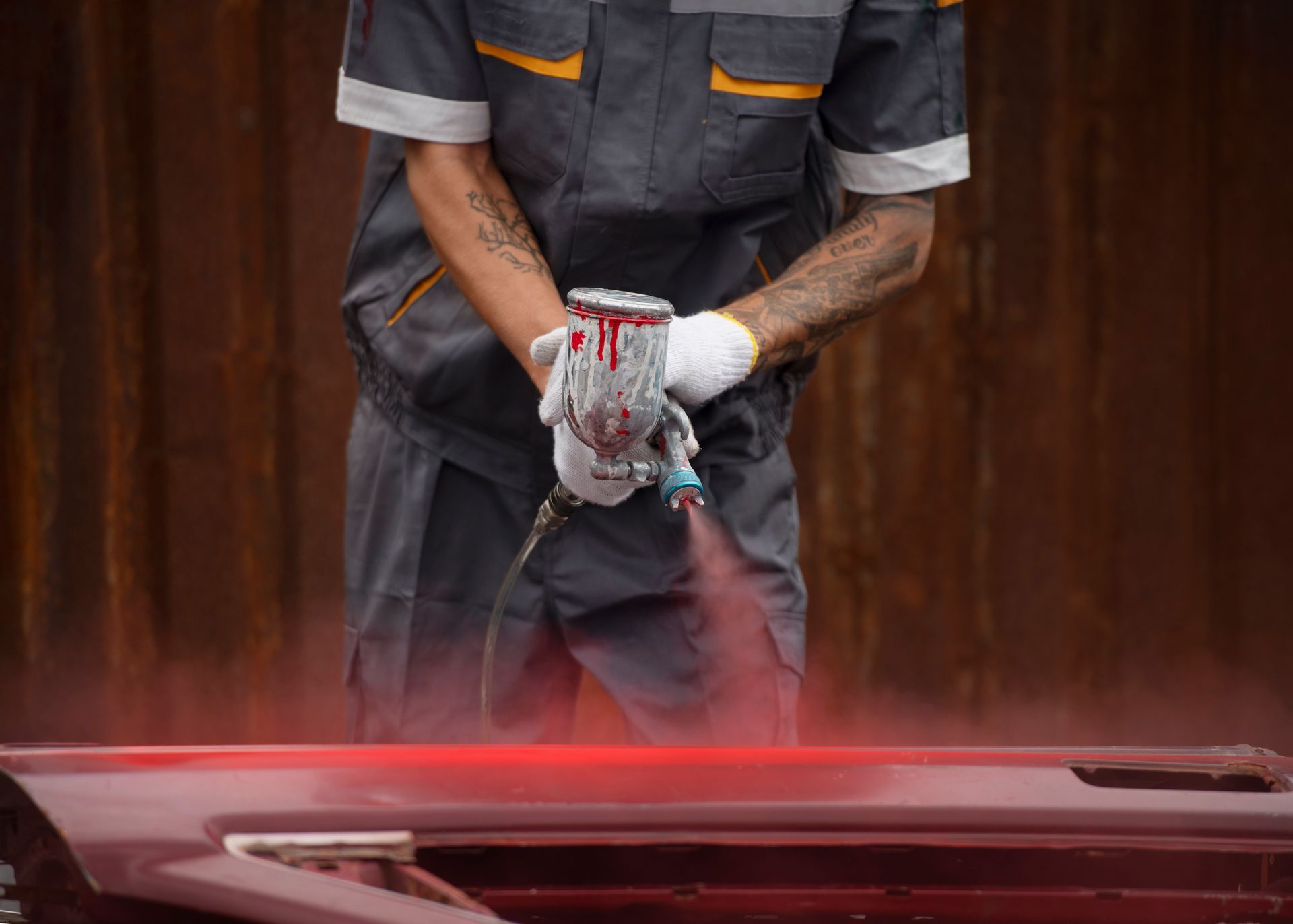Person in grey uniform spray-painting a car door red in a workshop.