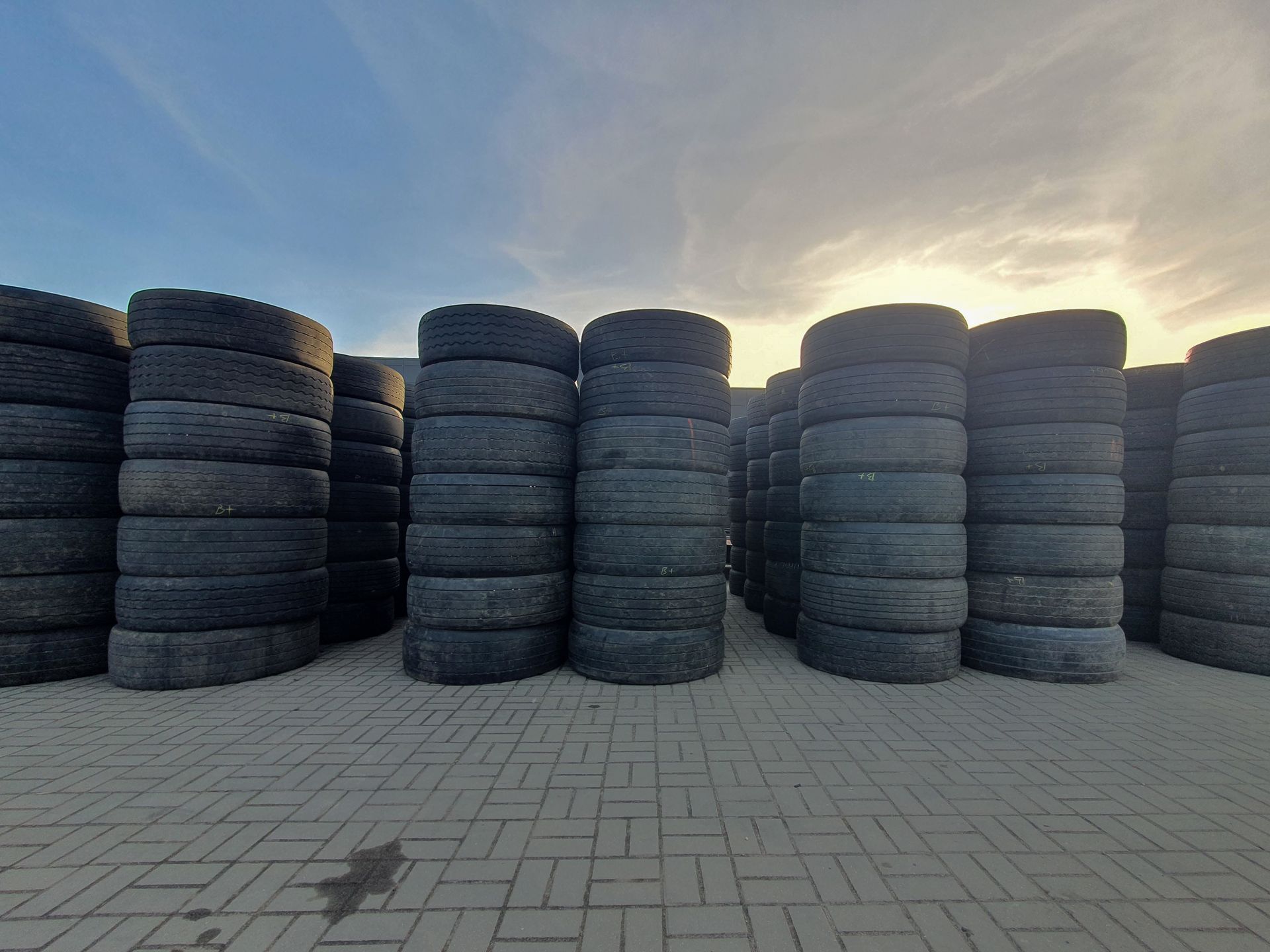Stacks of black tires on a paved surface under a blue and orange sky.
