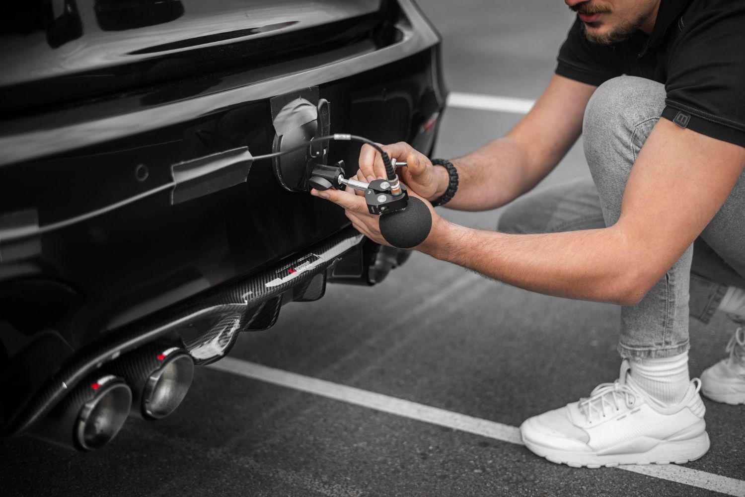 Man crouching to attach a trailer hitch to a black car in a parking lot