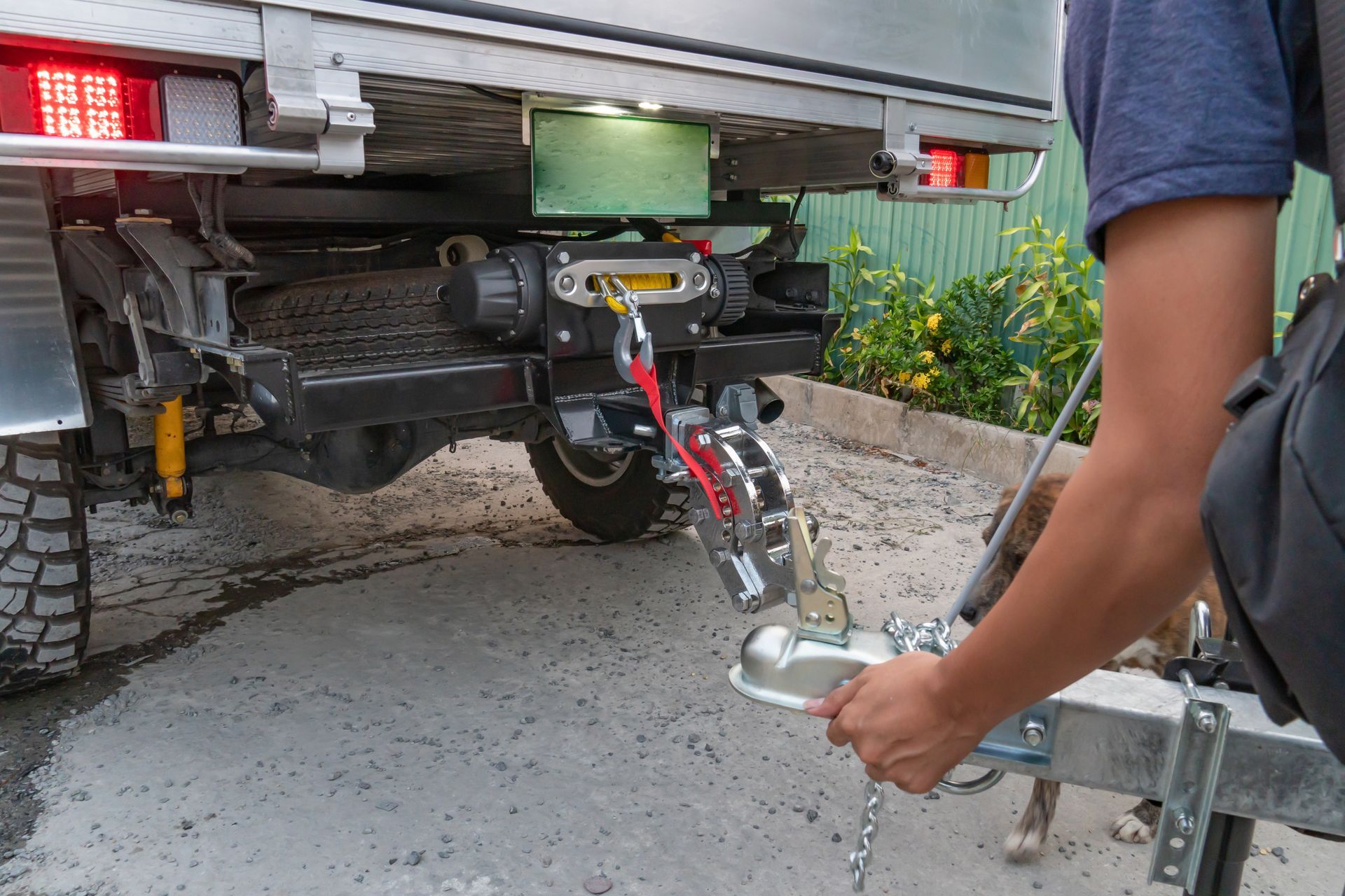 Person connecting a trailer to a vehicle with a winch, outdoors.