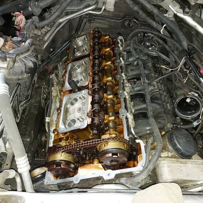 Car engine with exposed camshafts and timing chain, covered in oil, inside a vehicle.