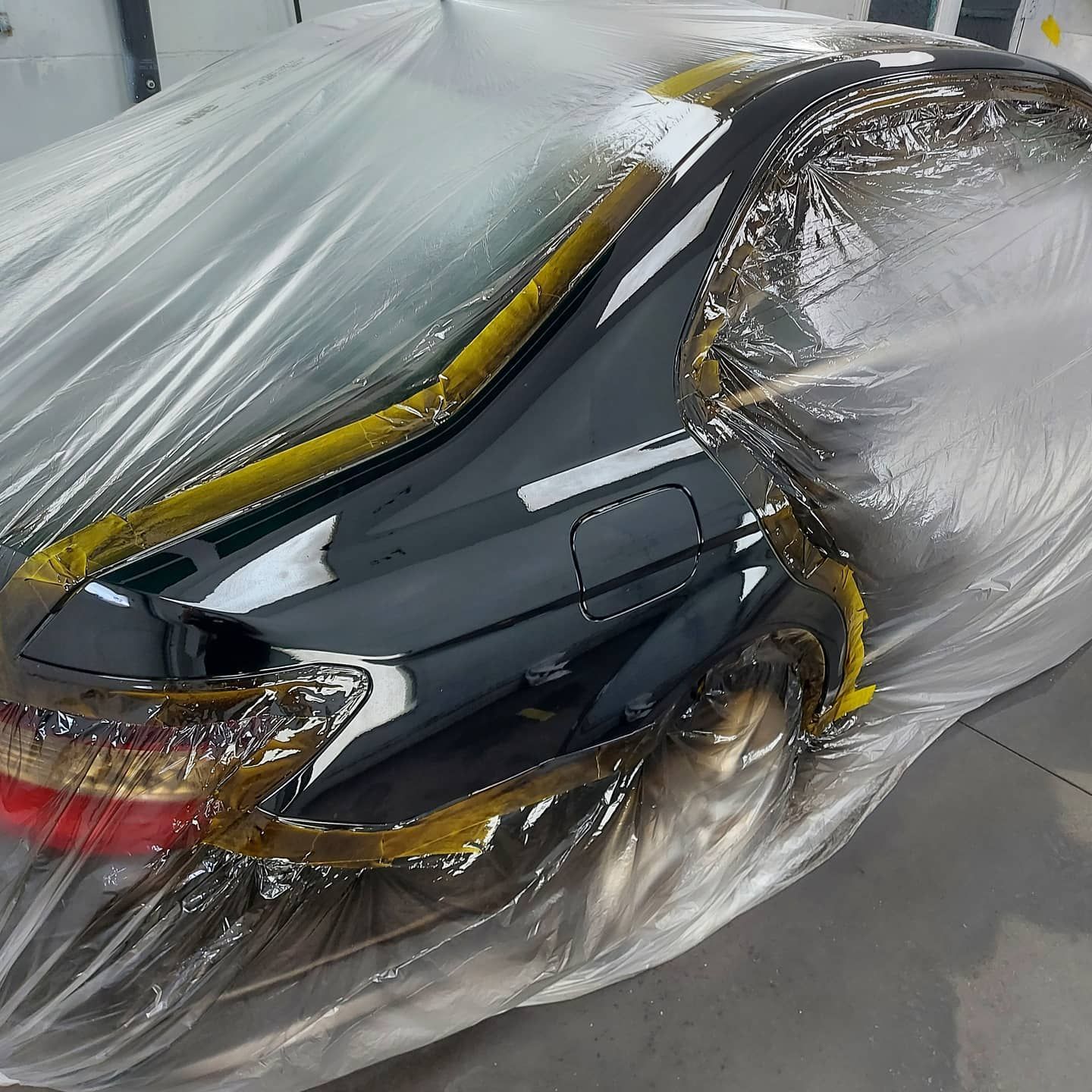 A black car is wrapped in plastic and ready to be painted