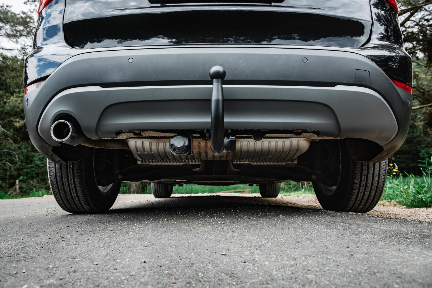 A black car with a tow hook attached to the back is parked on the side of the road.