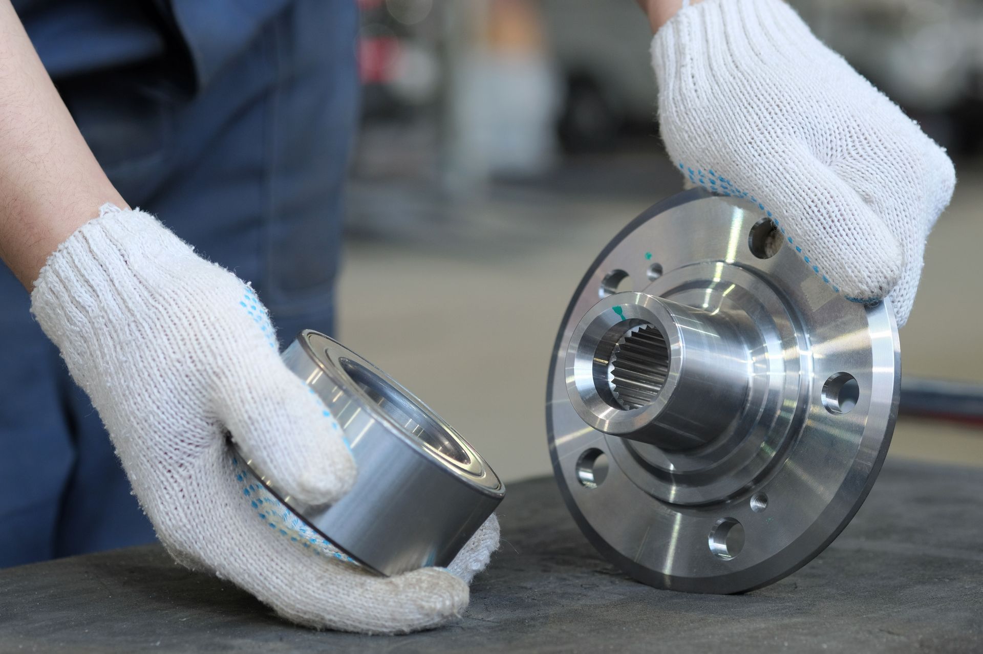 Hands in white gloves holding a metal wheel hub and a separate component in a workshop.
