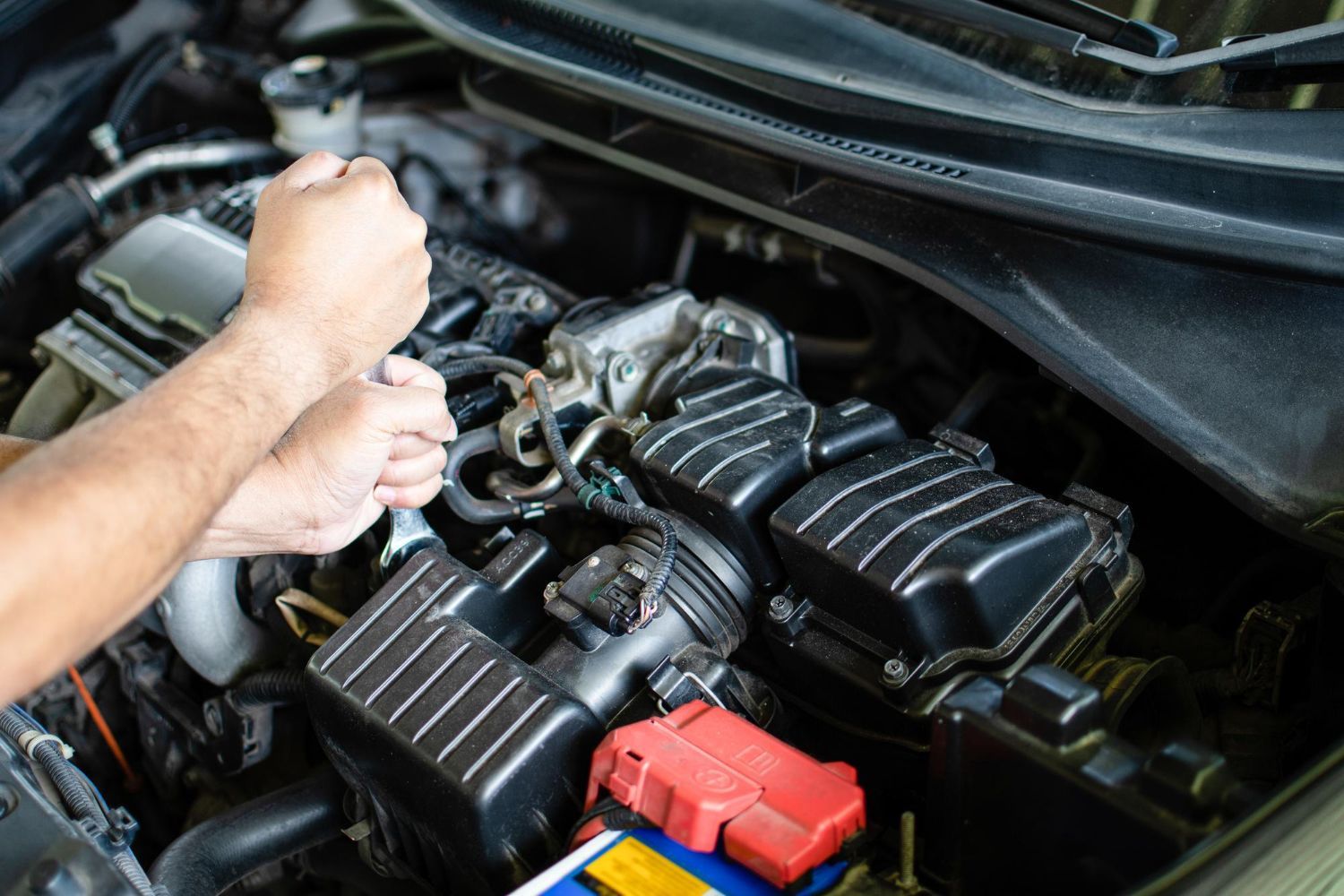 Person checking a car engine with a jump starter and battery in the engine bay