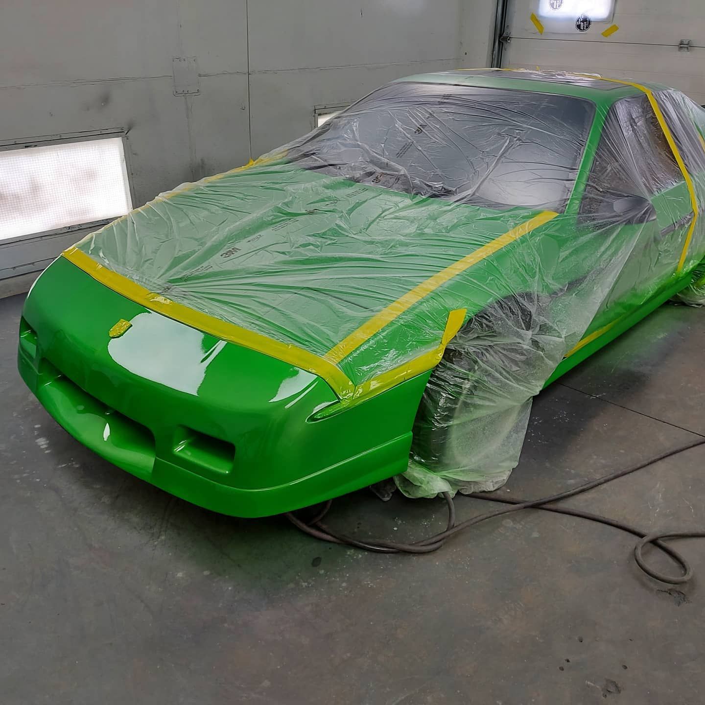 A green car is being painted in a garage.