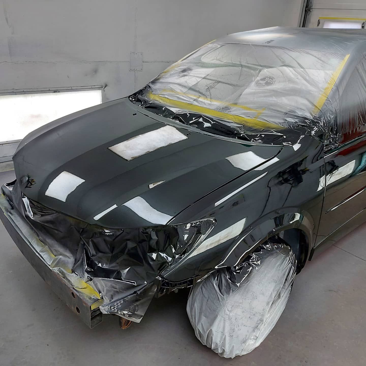 A black car is sitting in a garage covered in paint.