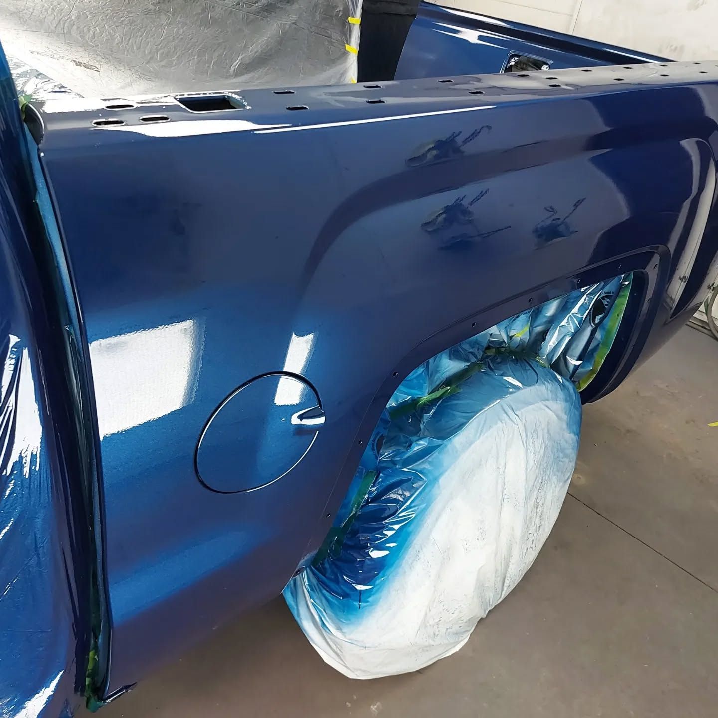 A blue truck is being painted in a garage