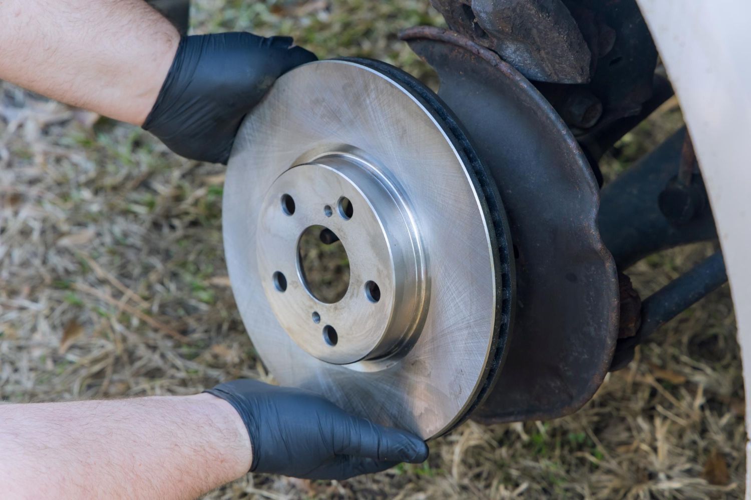 Gloved hands removing a car brake rotor from the wheel hub