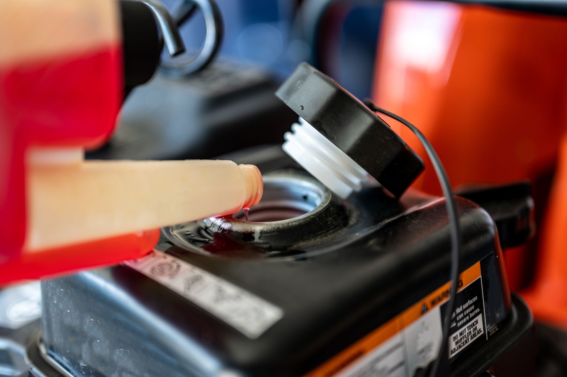 Fuel being poured into a small engine's fuel tank, with a red fuel container and funnel in use.