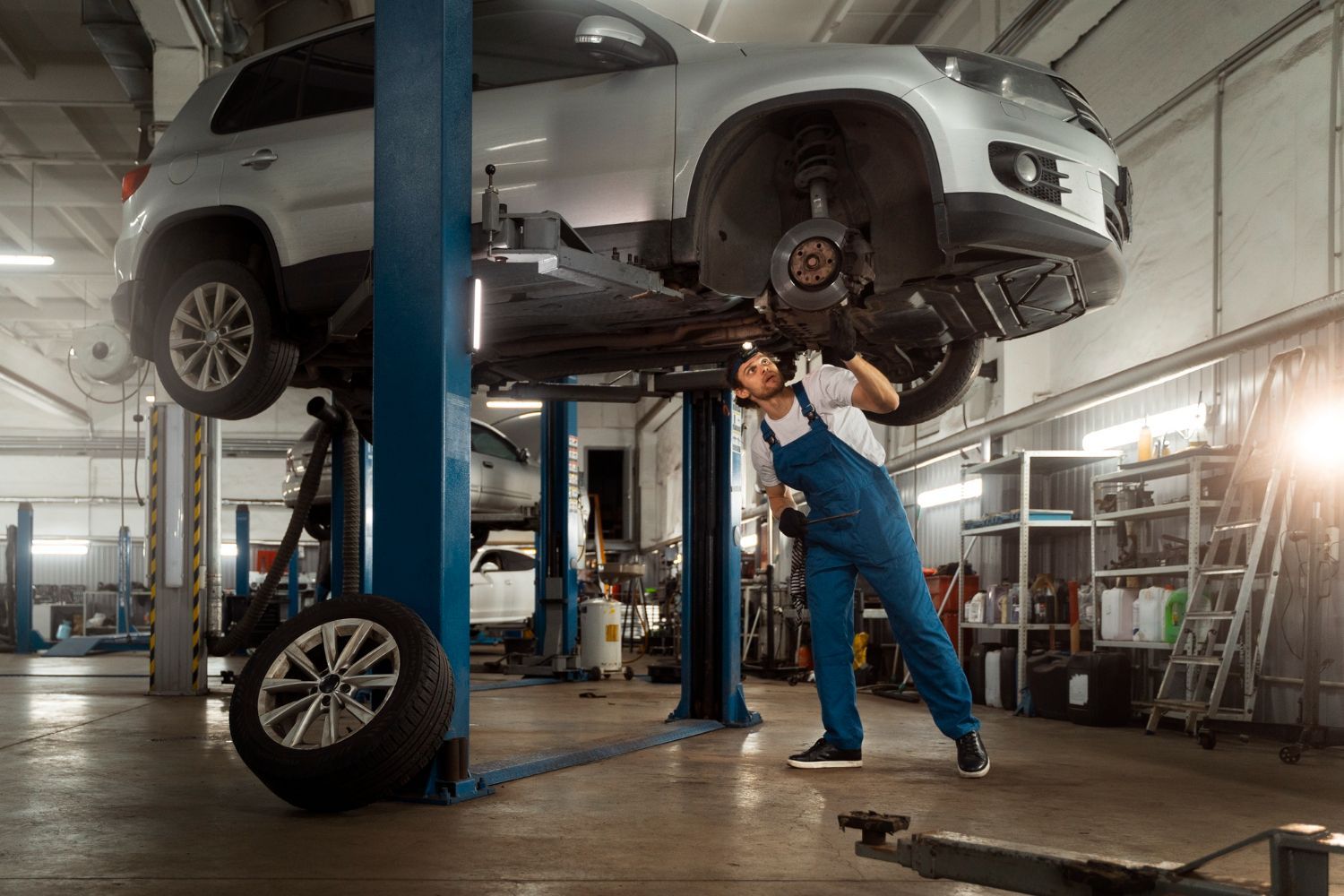 A mechanic is working on a car on a lift in a garage.