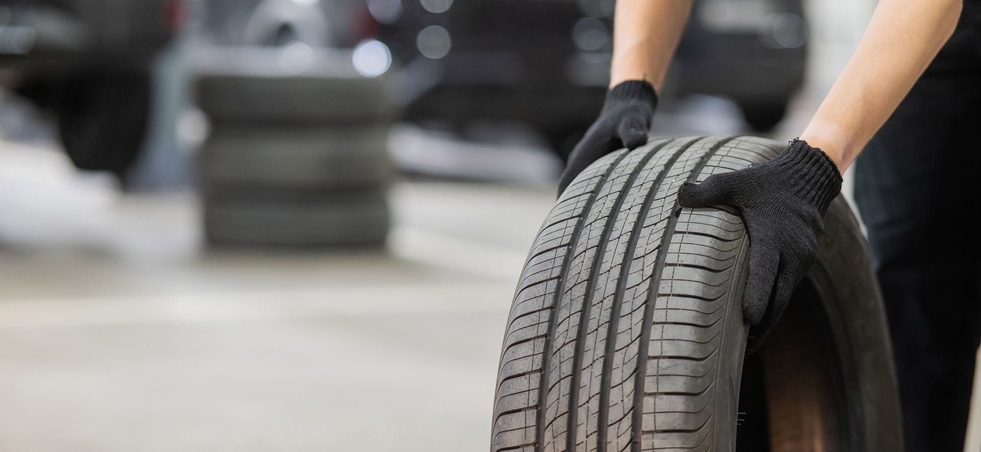 Person wearing black gloves handling a tire in a garage.