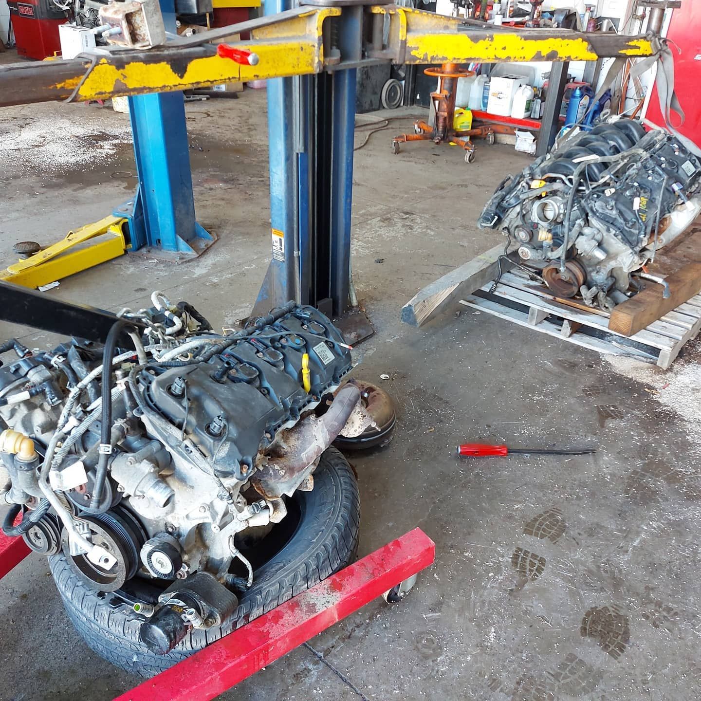 Two car engines sit on jacks in a repair shop. One engine sits on a tire.