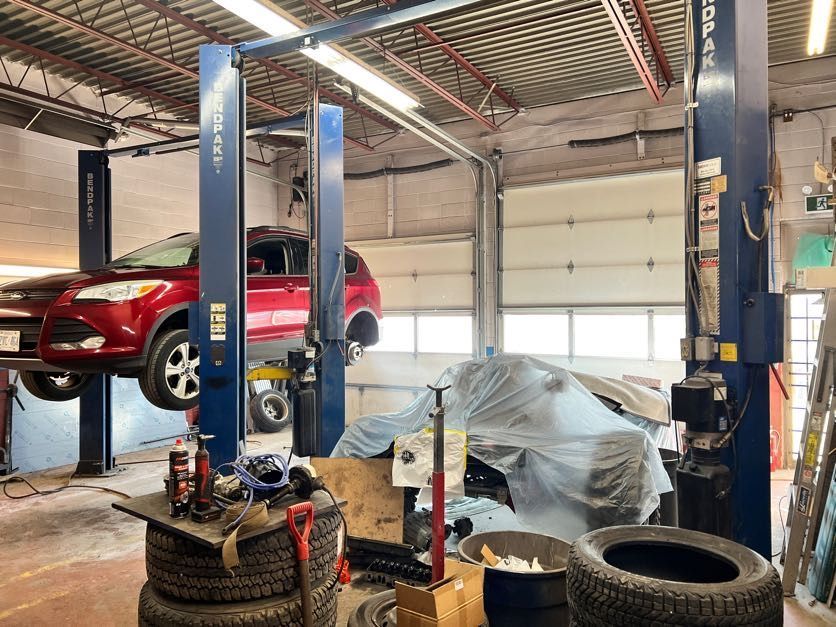 Red SUV on a car lift in a cluttered auto repair shop, with tools and tires visible.