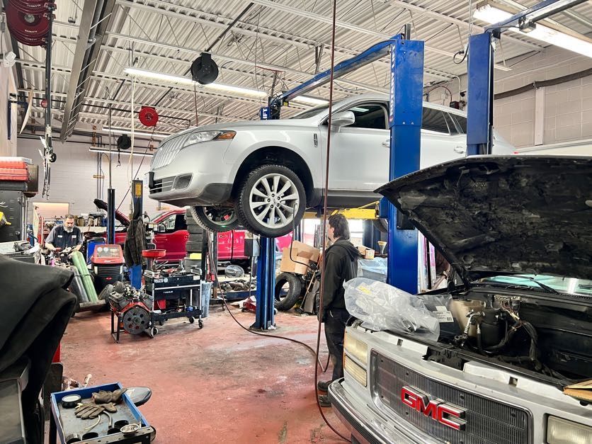Car in a mechanic shop raised on a lift; a mechanic works on a vehicle.