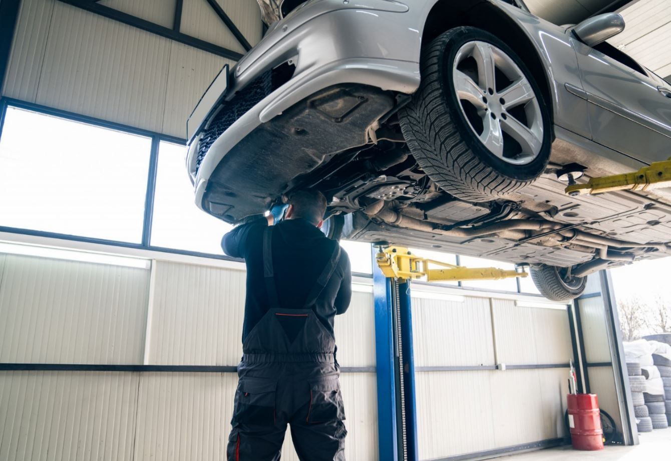 Mechanic working on the underside of a car lifted in a repair shop.