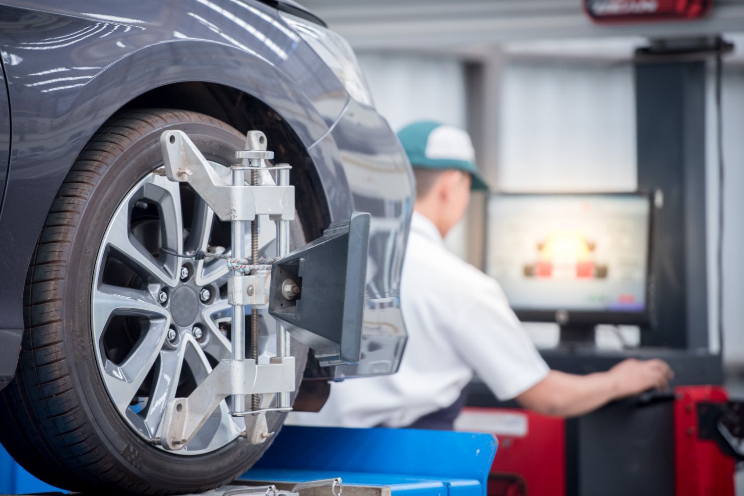 A man is working on a car wheel alignment machine in a garage.
