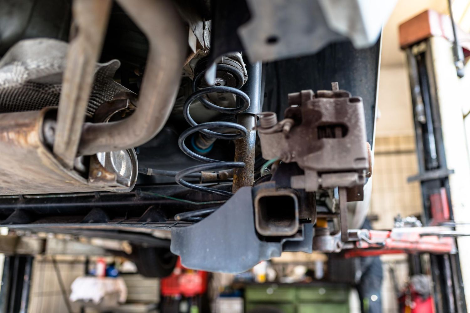 Undercarriage of a vehicle on a lift, showing suspension springs and exhaust components in a garage