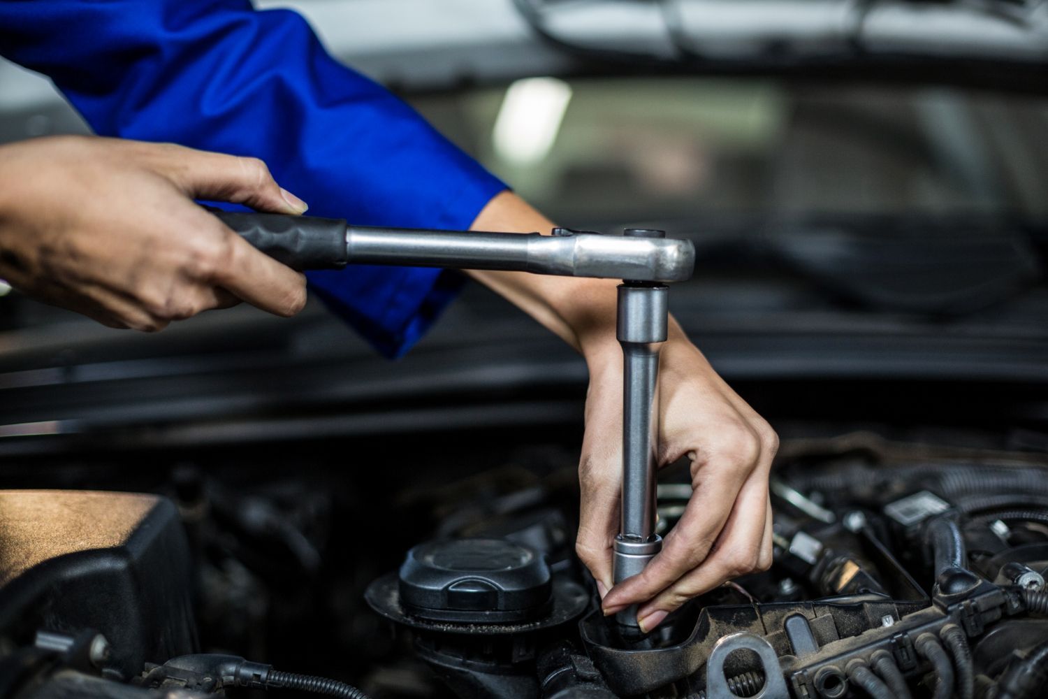 A person is working on a car engine with a wrench.