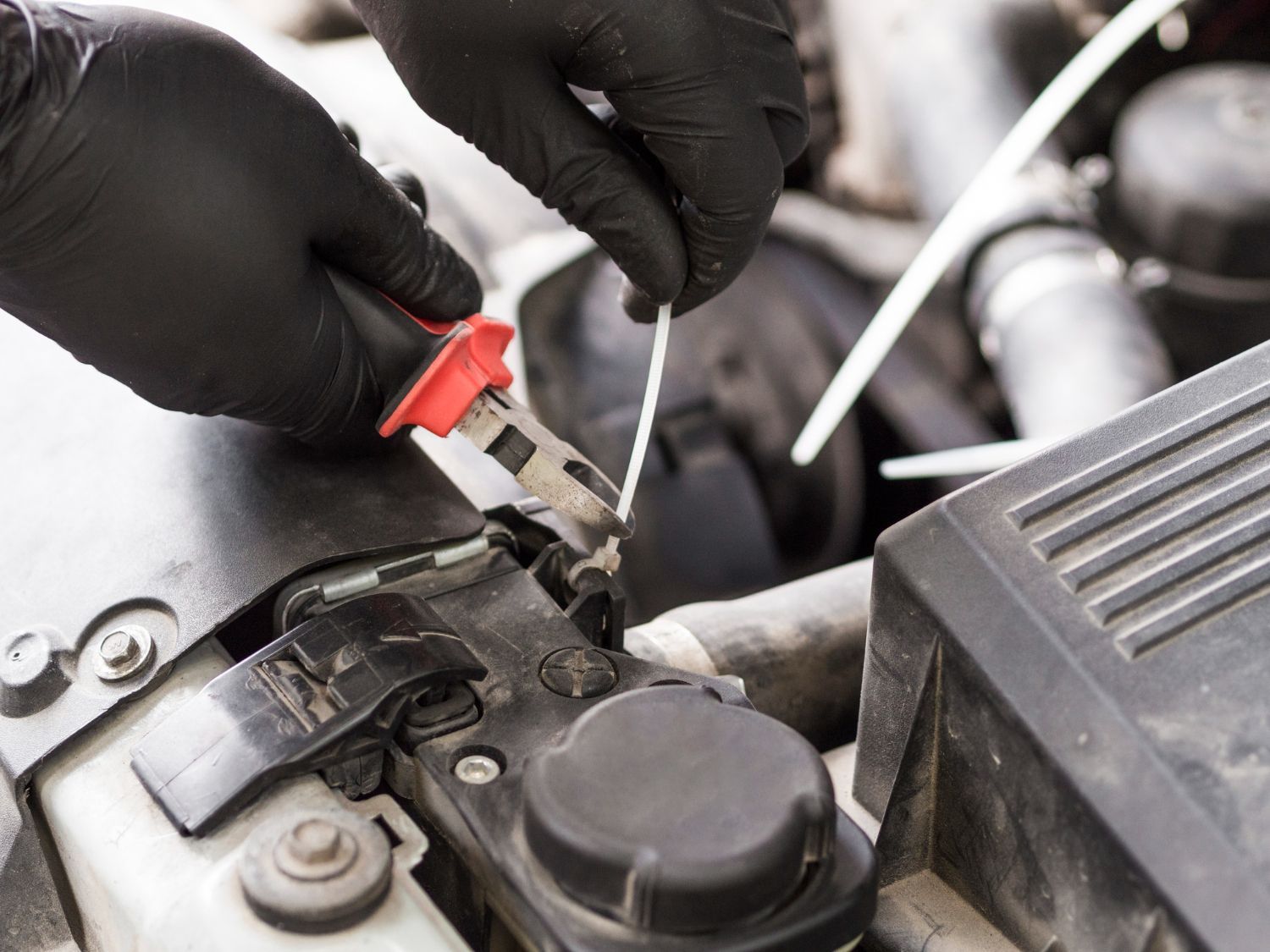 Gloved hands using pliers to connect a wire in a car battery compartment