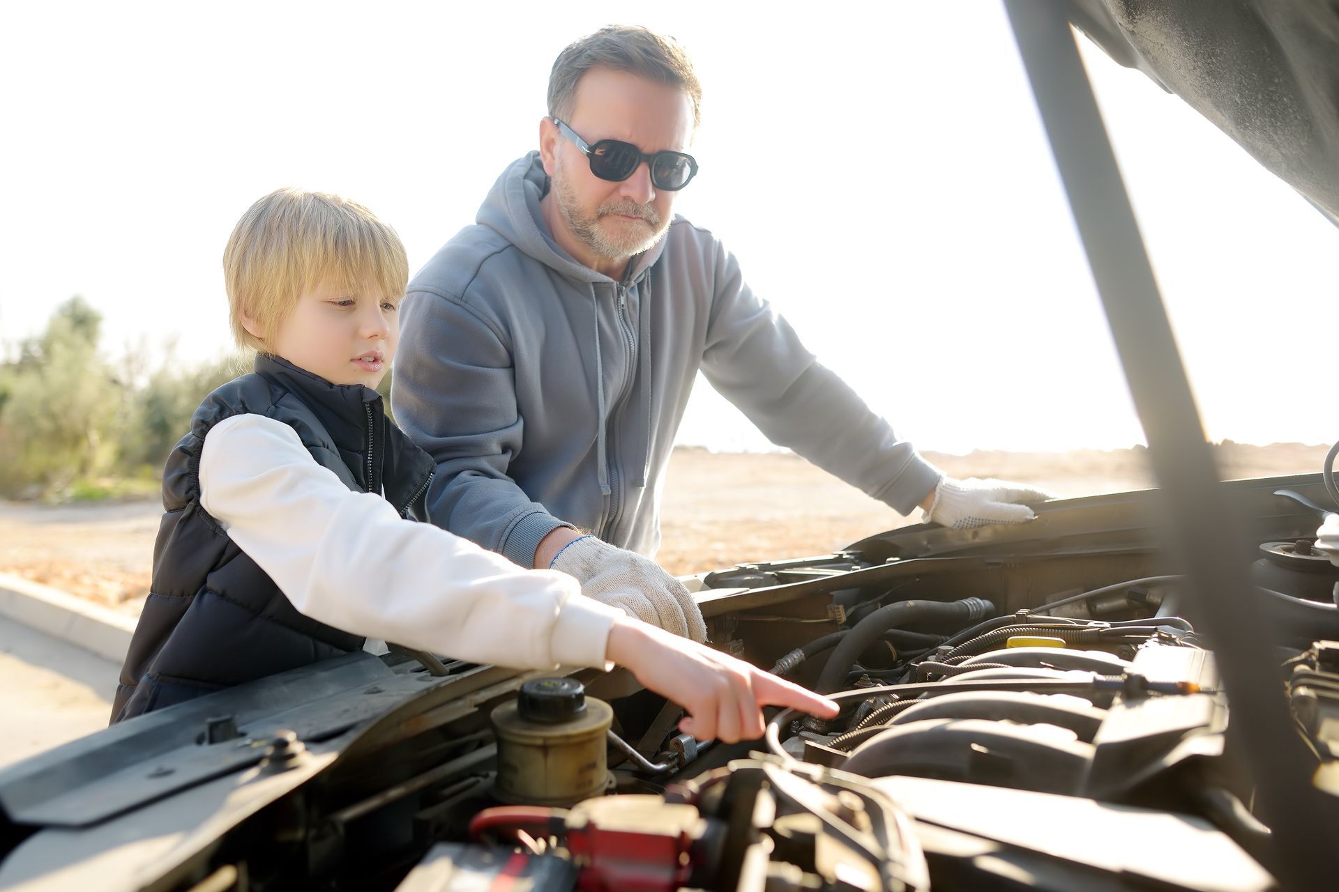 Man and child looking at car engine with open hood; child points at engine.